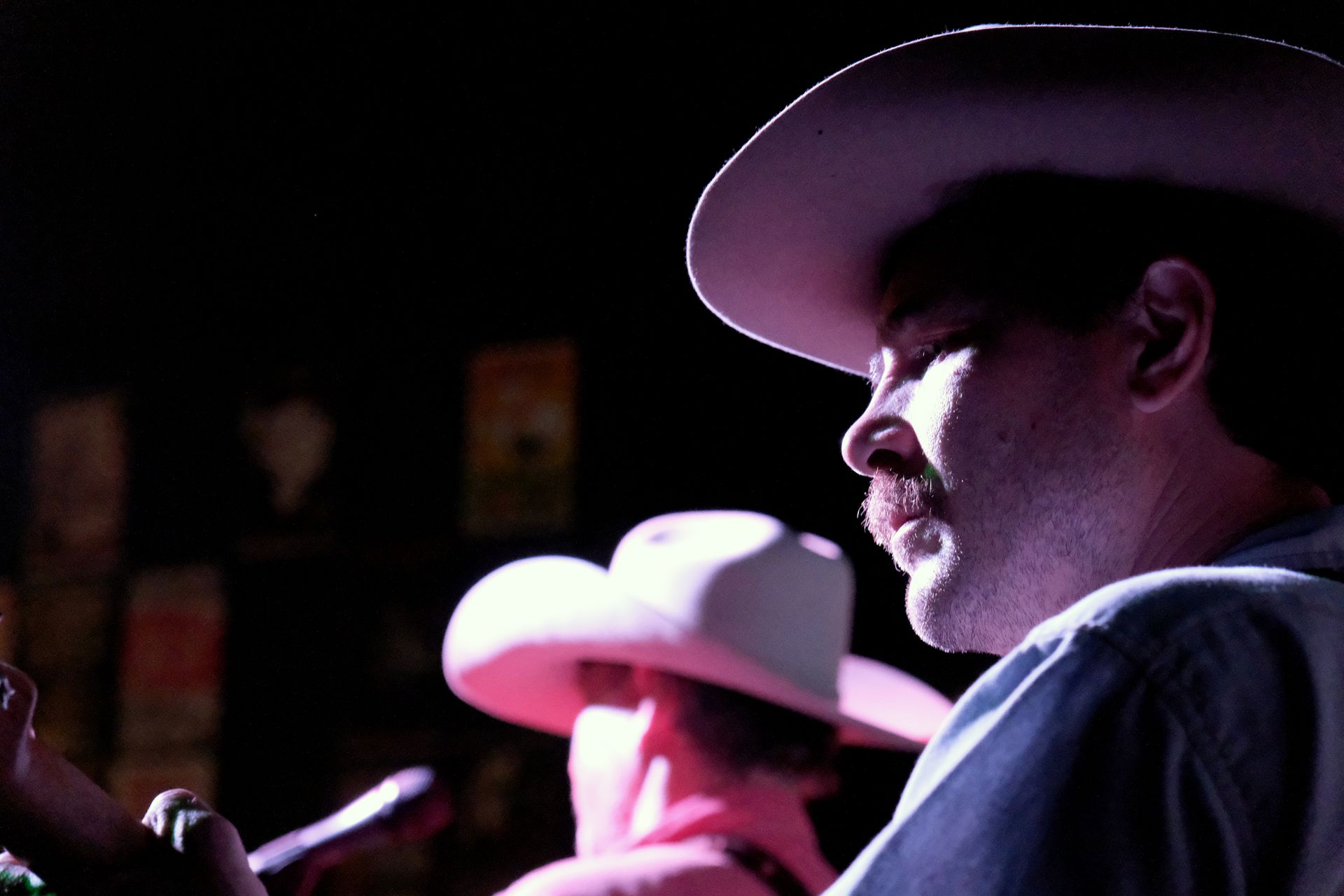 Two musicians wearing cowboy hats, one singing into a microphone. Dark stage, bright lighting.