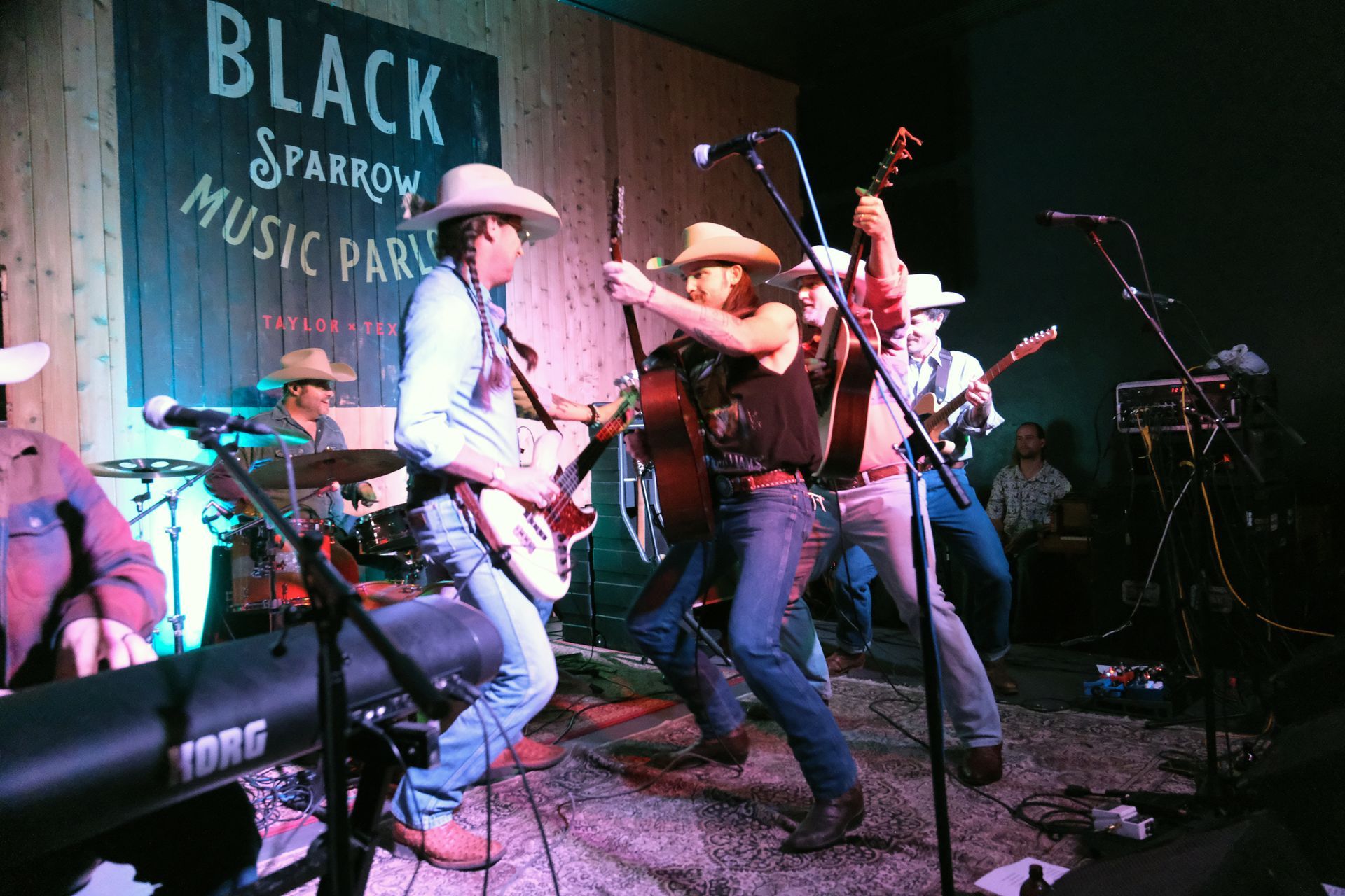 Band performing live at Black Sparrow Music Parlor; musicians in cowboy hats, playing guitars, keyboards, and drums.