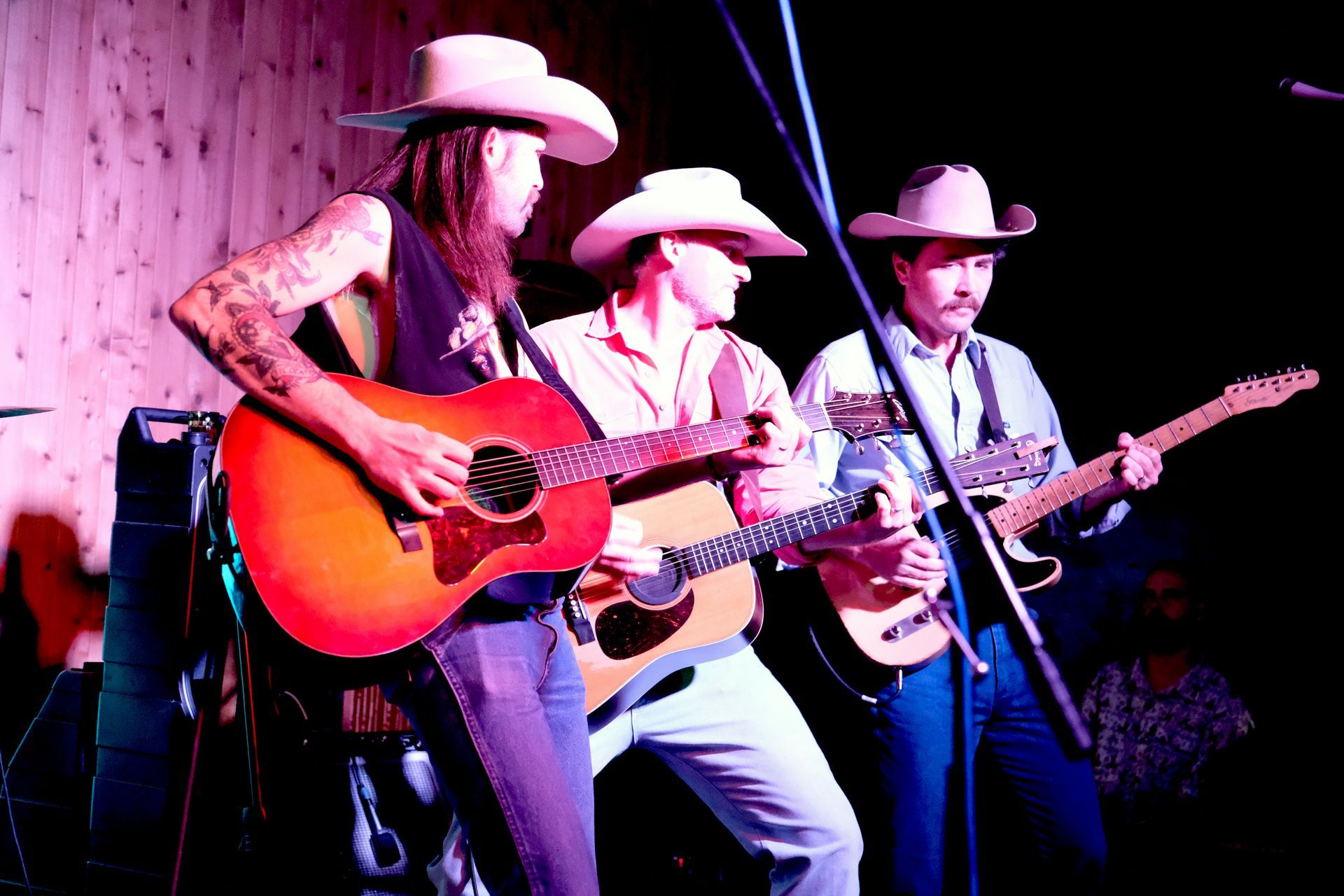 Three musicians in cowboy hats play guitars on stage.