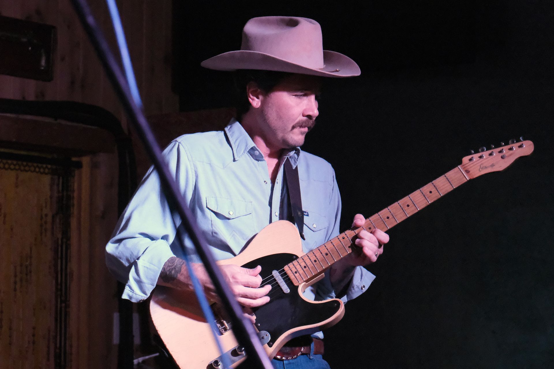 Man in cowboy hat playing an electric guitar in a dim setting.