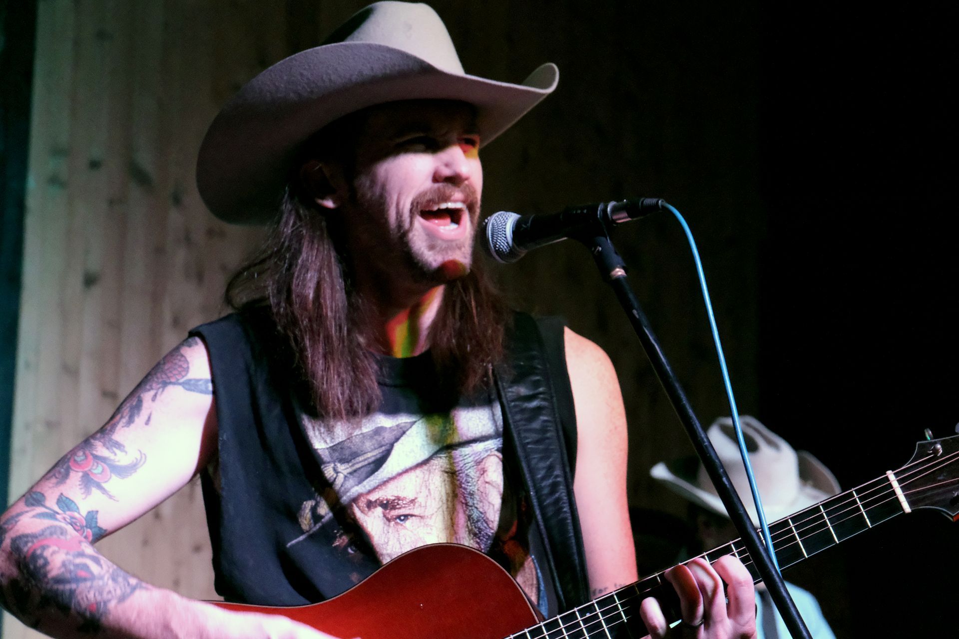 Man with cowboy hat singing and playing guitar on stage.