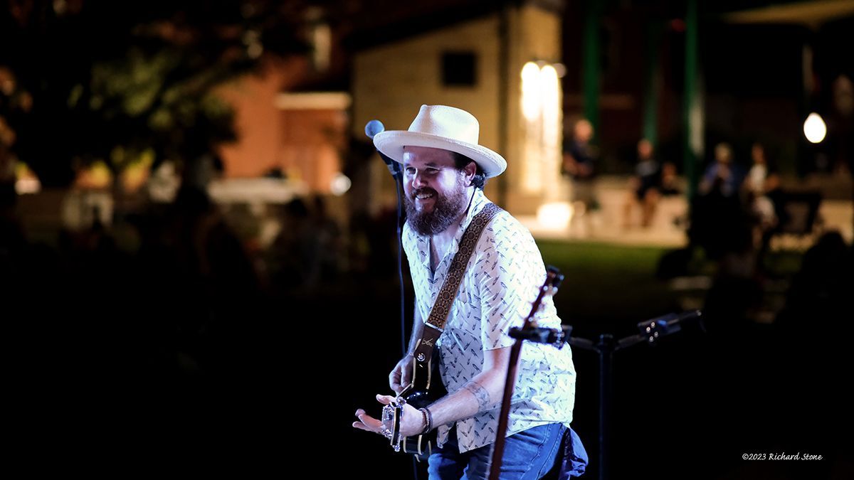 Man in hat playing guitar on stage at night.