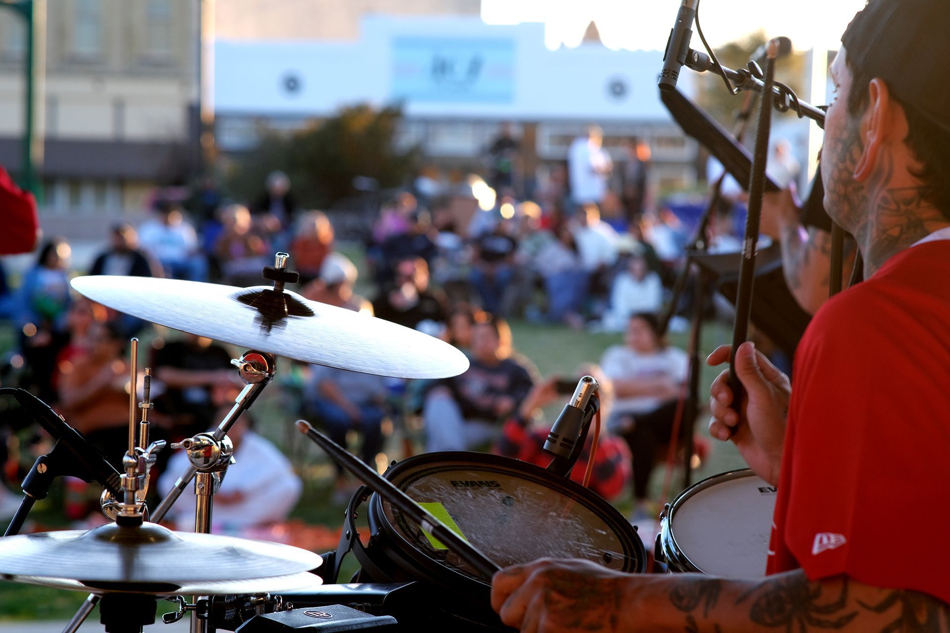 Drummer playing live music outdoors for a crowd.  Sunset lighting.