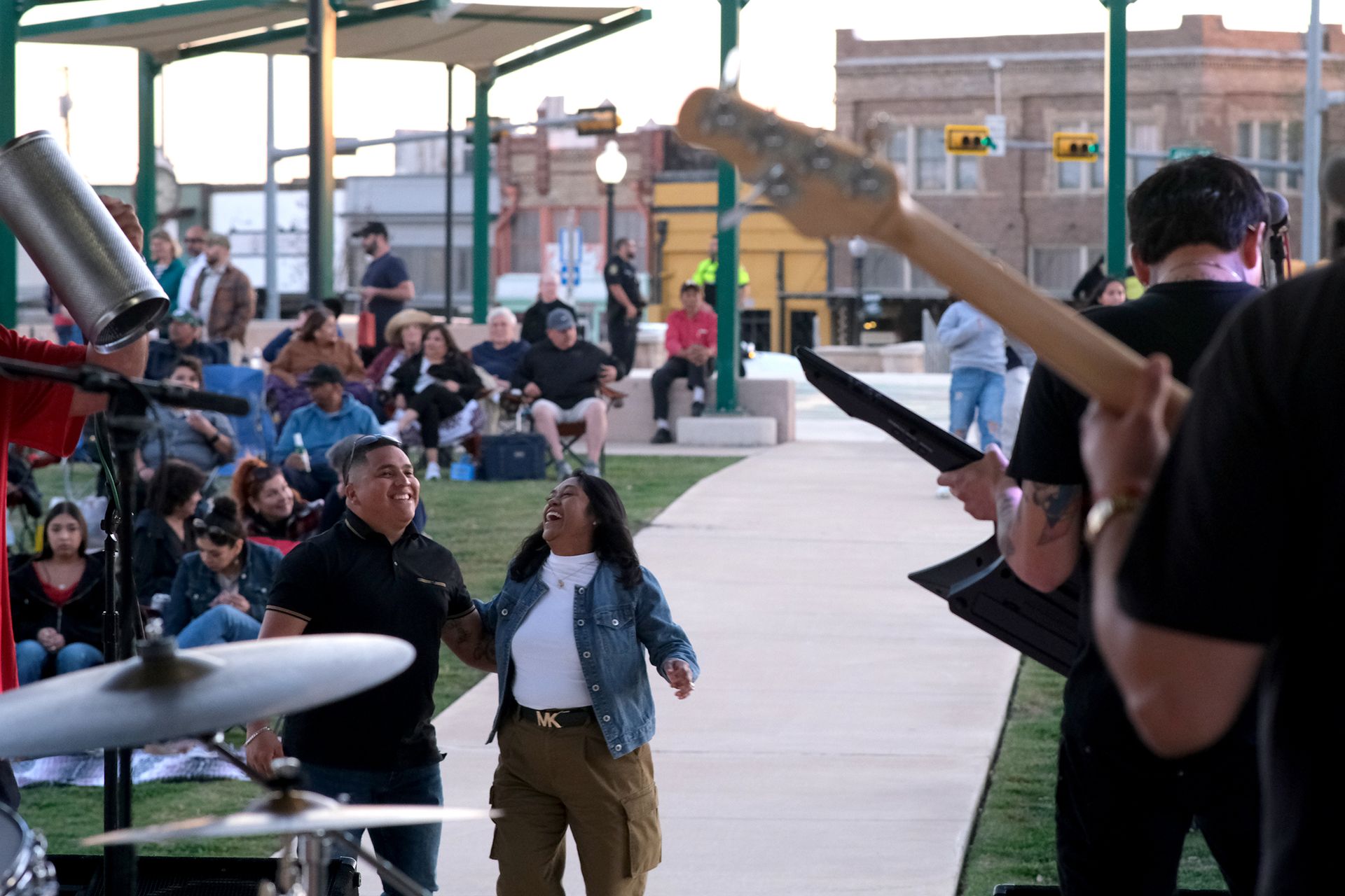Band performing outdoors for a crowd. People watch and two individuals dance, one smiling and singing.
