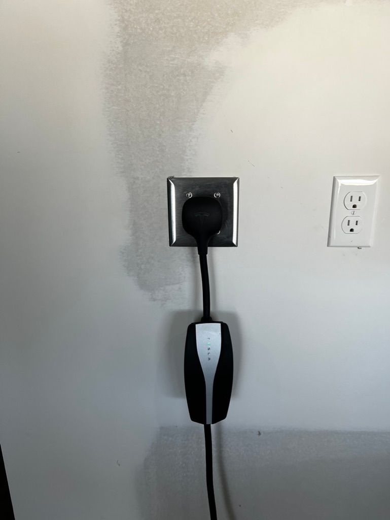 A tesla charging station is plugged into a wall outlet.