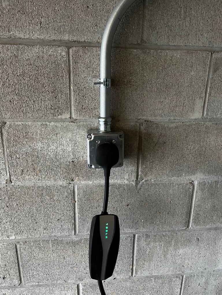A tesla charging station is attached to a brick wall.