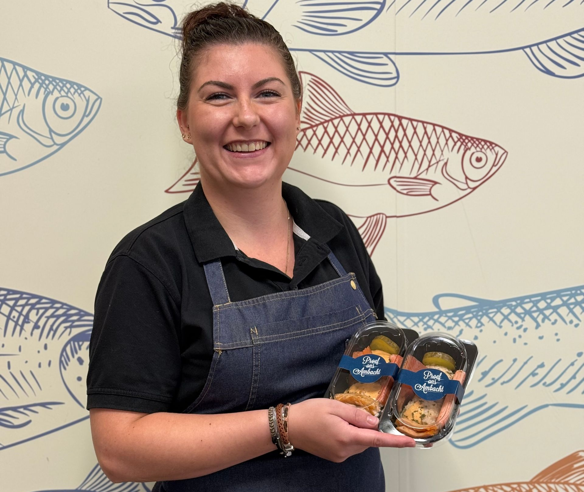 Een glimlachend persoon met een spijkerovertrek aan houdt twee bakjes met bereide zeevruchten