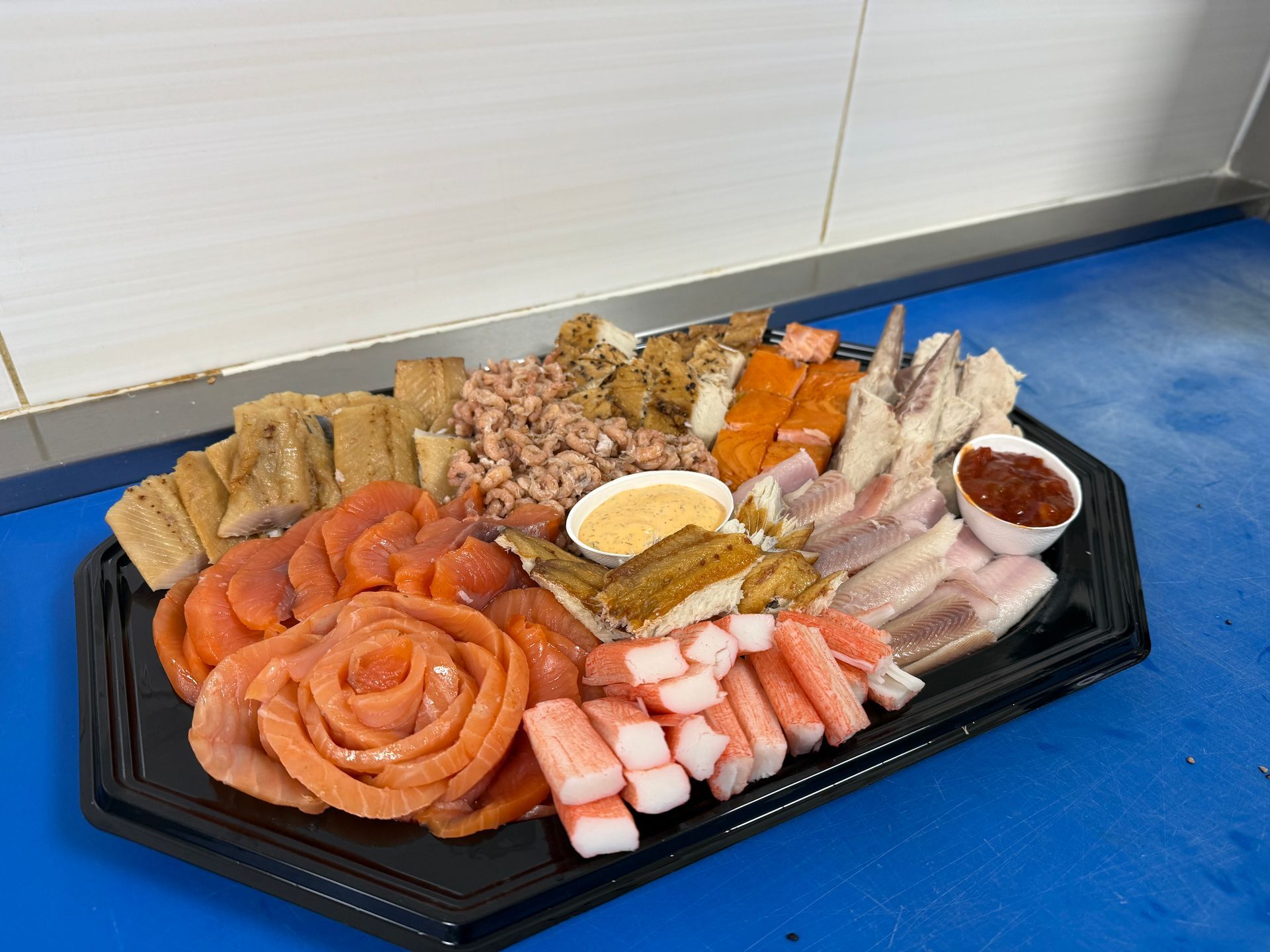 Een schotel met diverse soorte waaronder gerookte zalm, krabsticks en paling, met twee dipsauzen