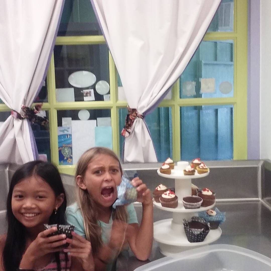 Two young girls are standing in front of a cupcake stand