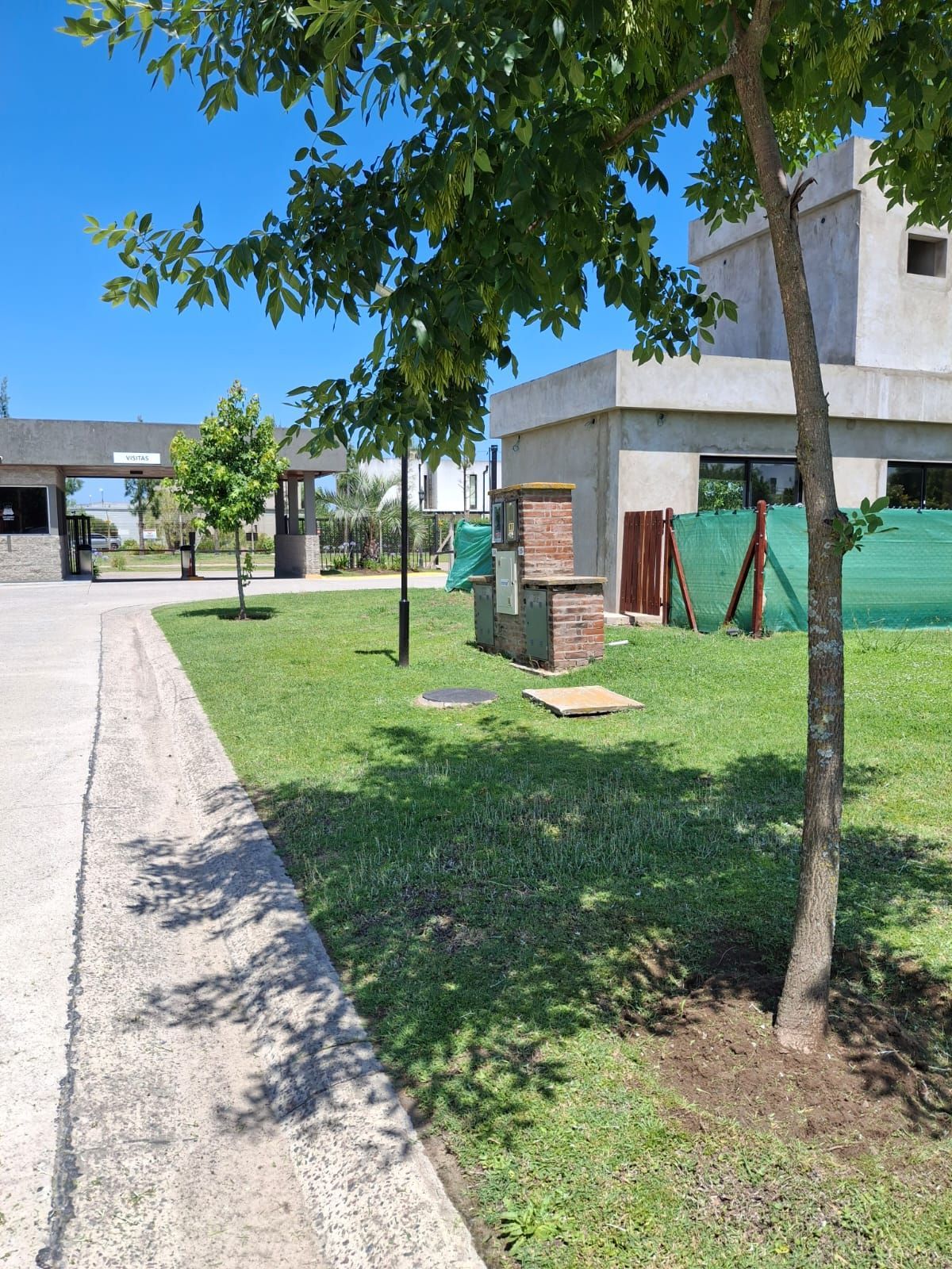 Vista exterior de una zona verde con árboles, un pilar de ladrillo y un moderno edificio