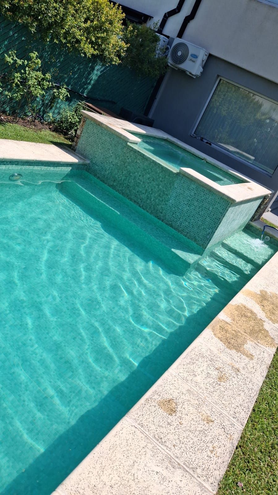 Una piscina de color turquesa con un jacuzzi alicatado adjunto, situada junto a un edificio