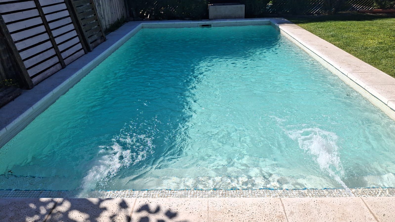 Una piscina rectangular en el patio trasero, con agua azul claro y dos chorros sumergidos que crean ondas