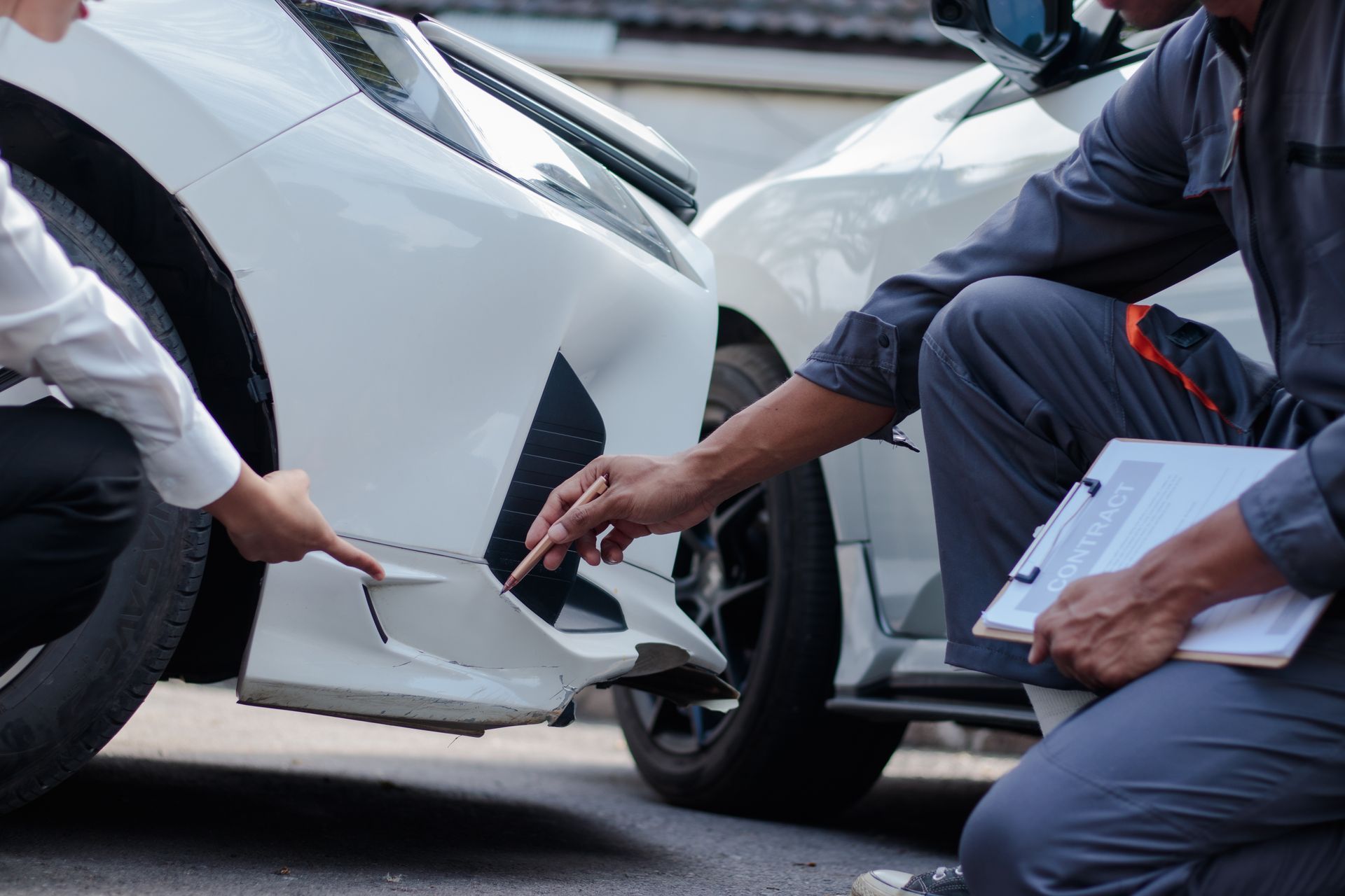 Two people inspecting damage to a white car’s front bumper after a collision