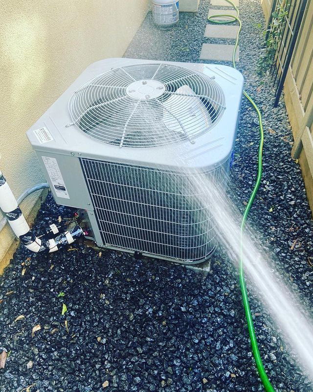 A hose is spraying water on an air conditioner.