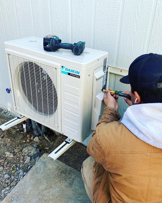 A man is working on an air conditioner outside of a building.