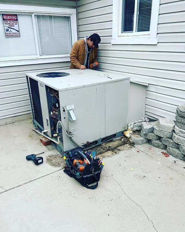 A man is working on an air conditioner outside of a house.