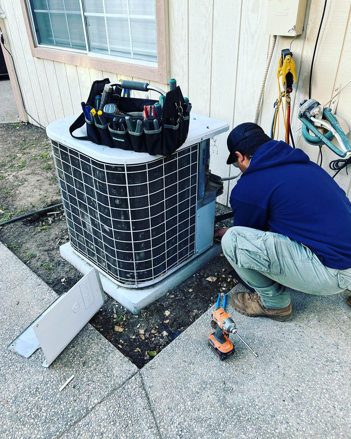 A man is working on an air conditioner outside of a house.