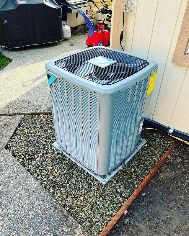 A large air conditioner is sitting on top of a gravel area next to a building.