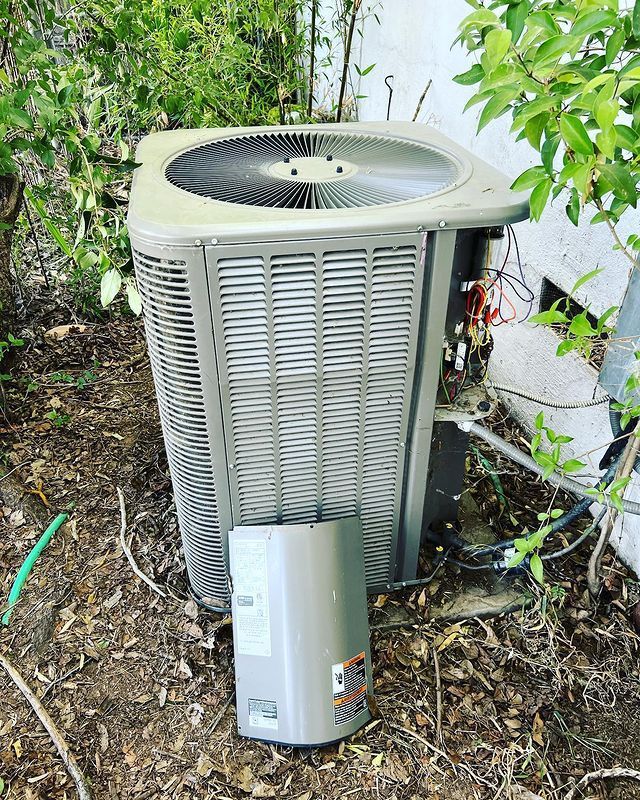 An air conditioner is sitting on the ground next to a hose.