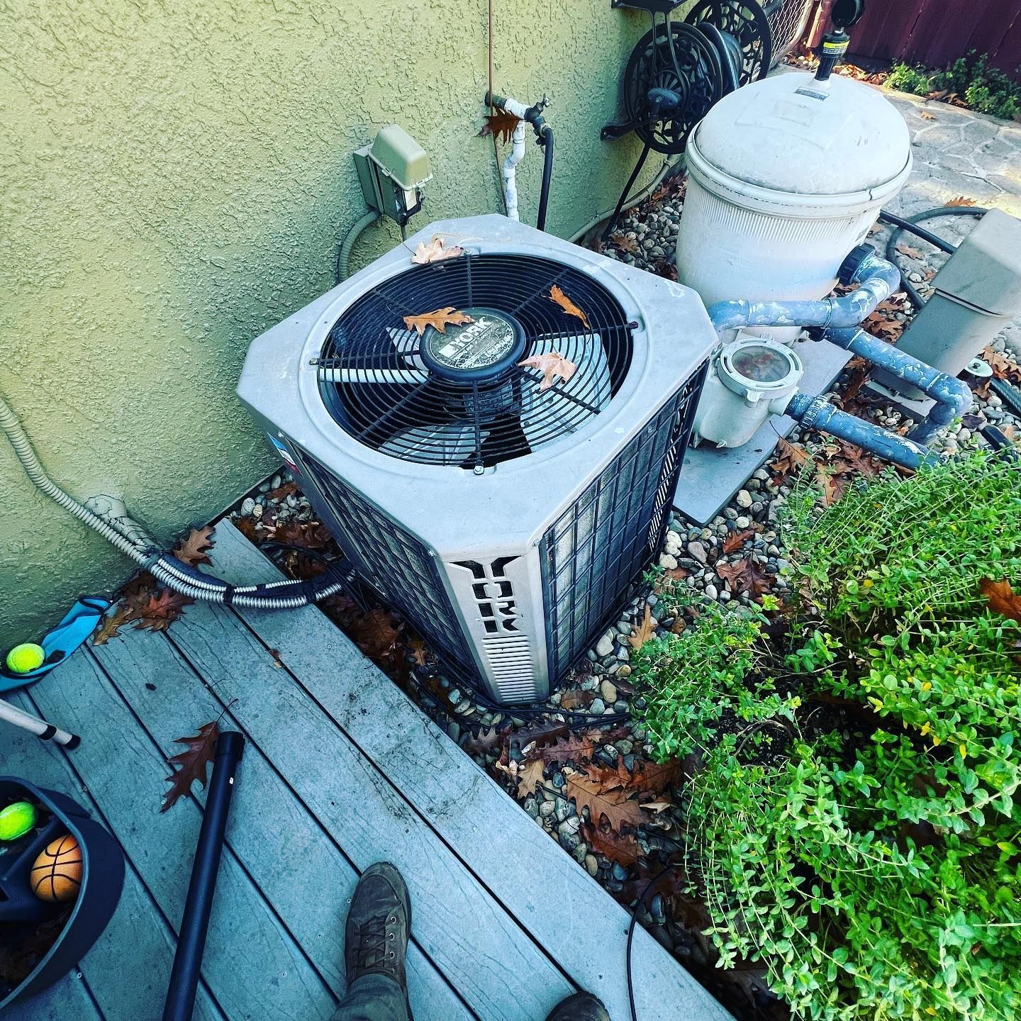 An air conditioner is sitting on a deck next to a pool filter.