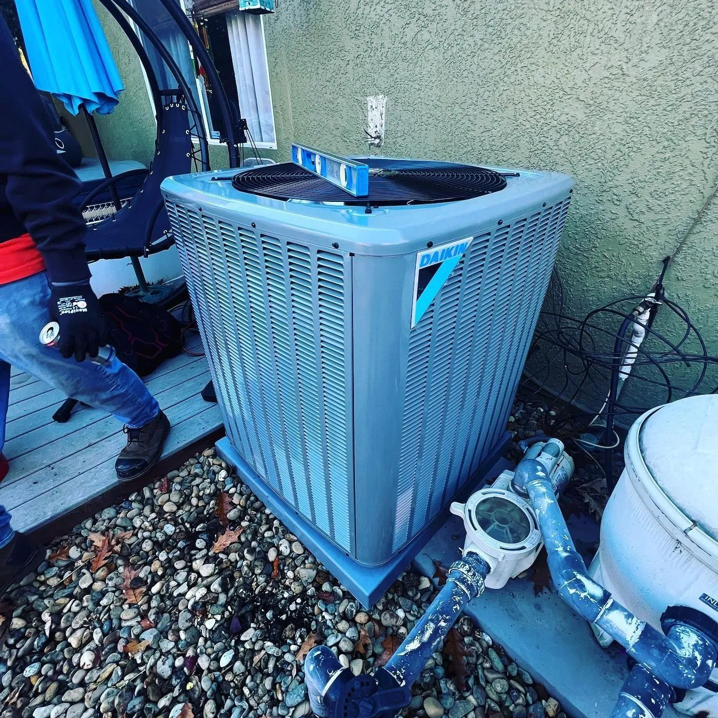 HVAC unit next to a wall, pool equipment, and a person wearing blue jeans.