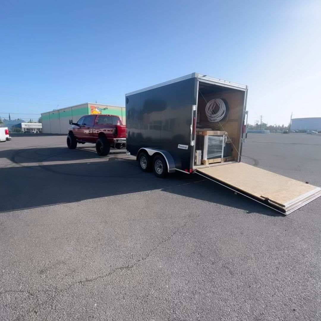 A red truck is towing a black trailer in a parking lot.