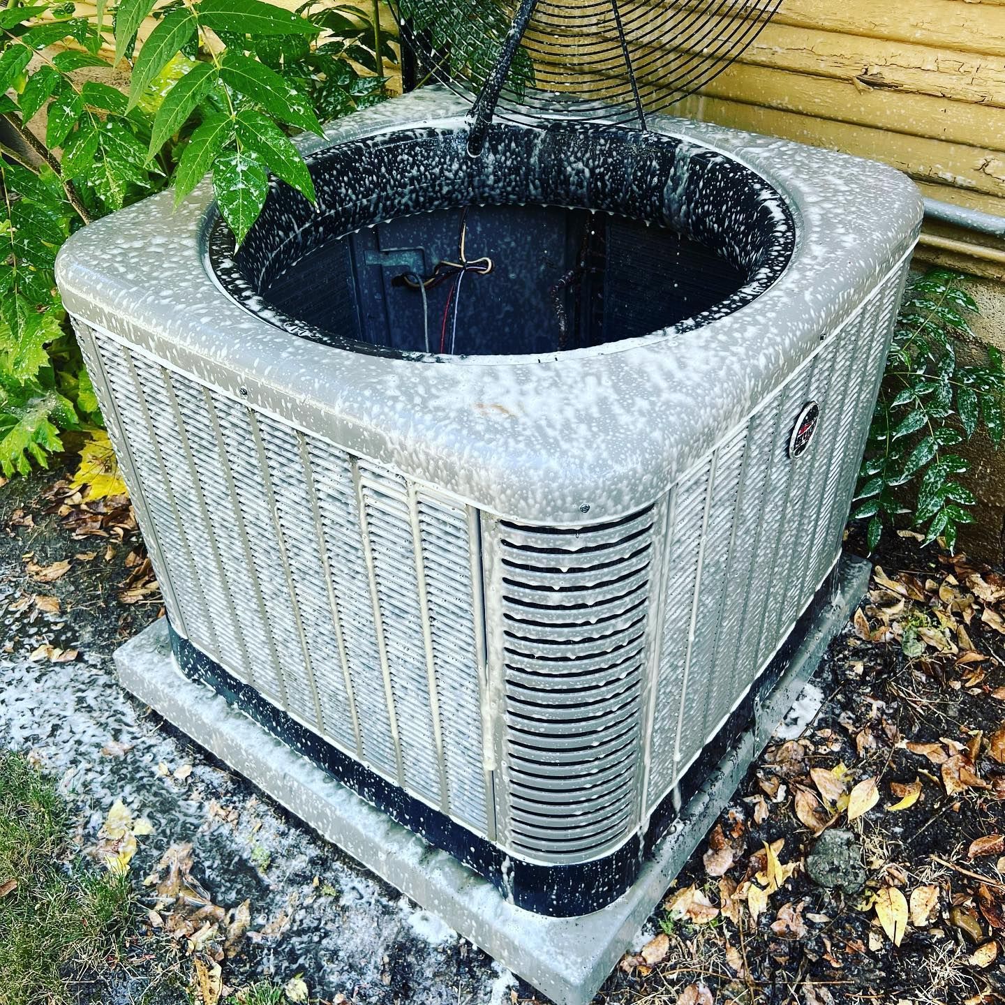 A dirty air conditioner is sitting on the ground next to a house.