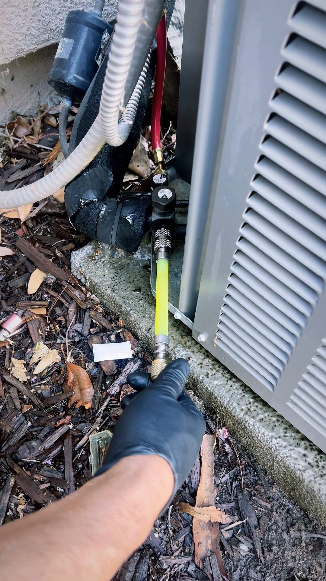 A person is holding a yellow hose in front of an air conditioner.