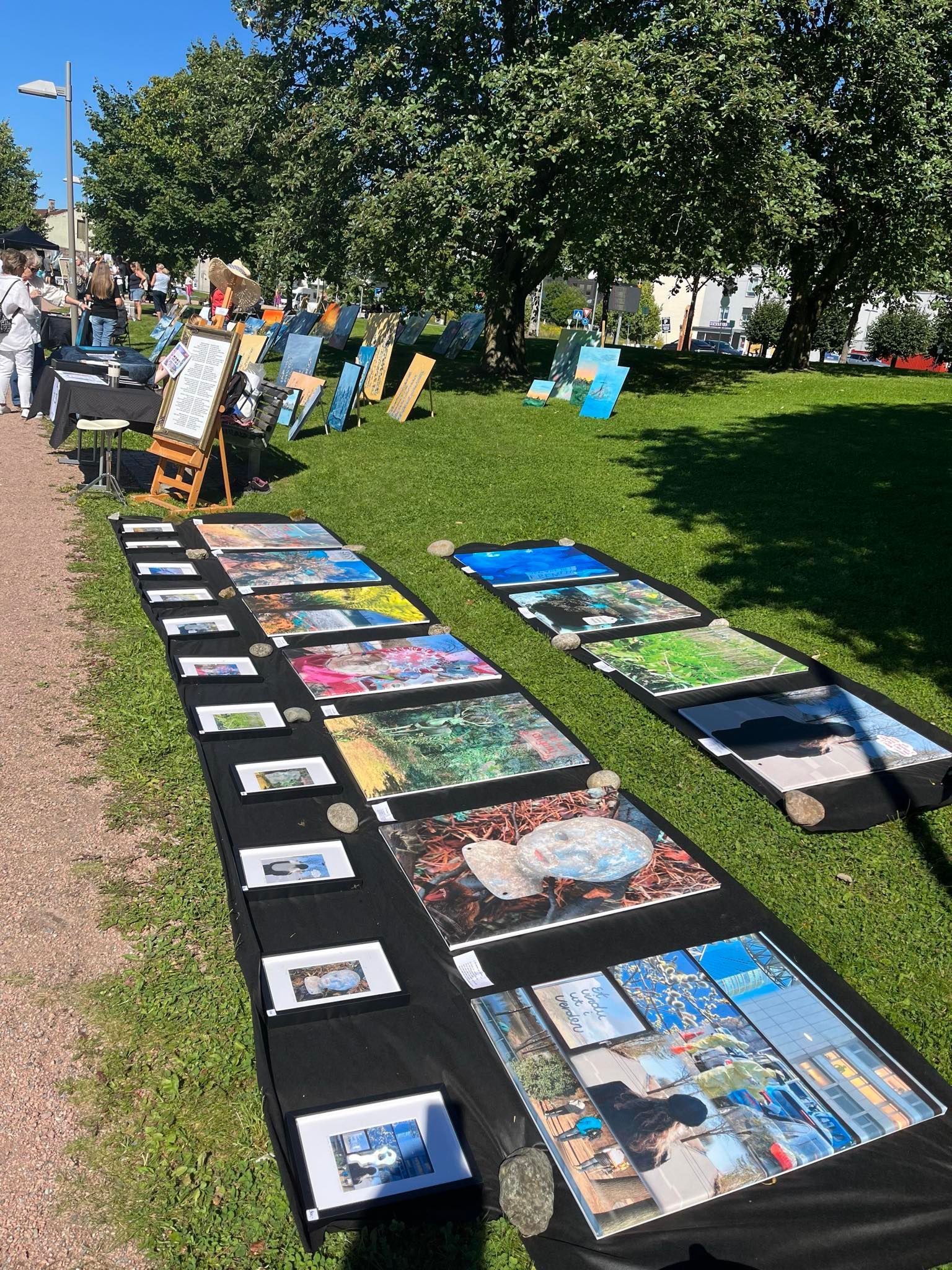 En rad med malerier sitter på et bord i en park.