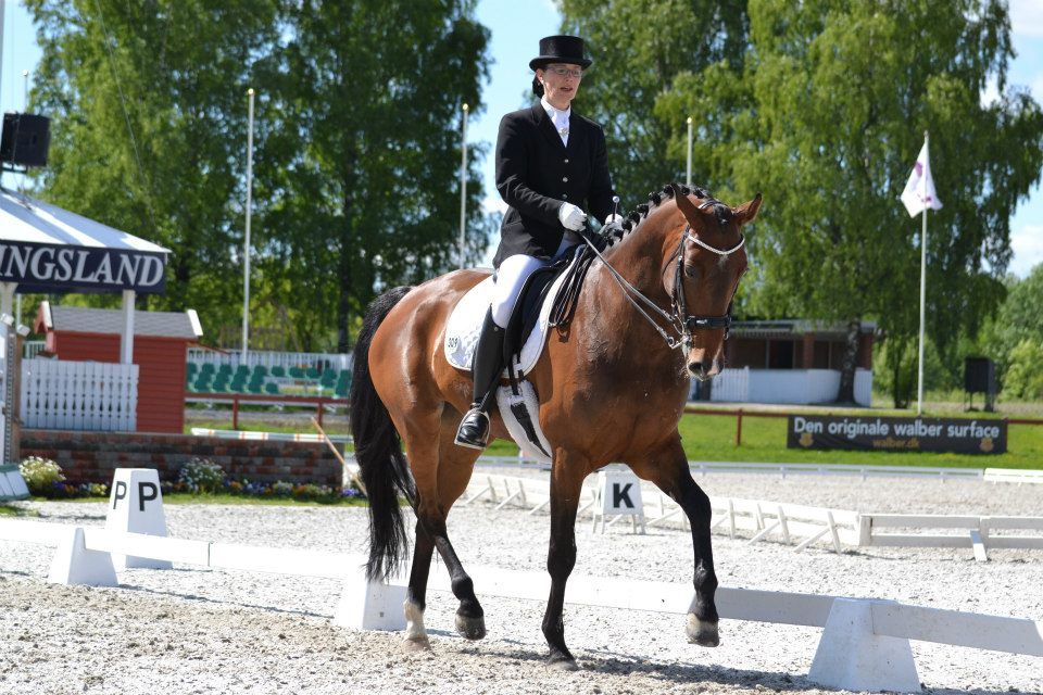 En kvinne rir på en brun hest foran et skilt som sier kingsland