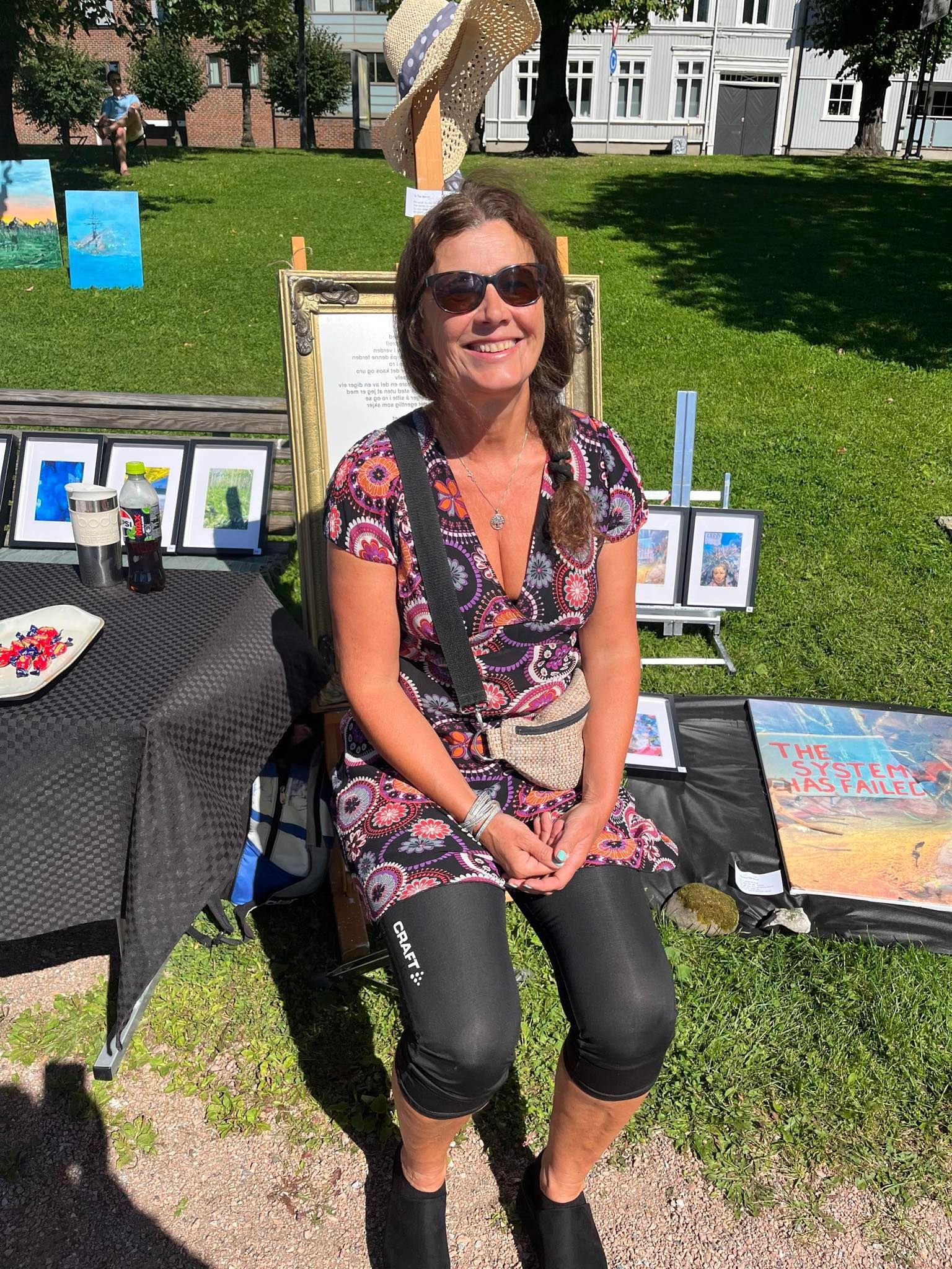 En kvinne med solbriller sitter i gresset foran et bord.