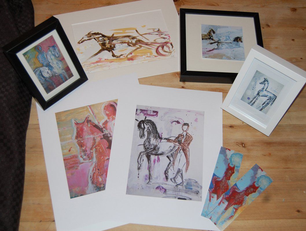 Flere innrammede hestemalerier står på et trebord