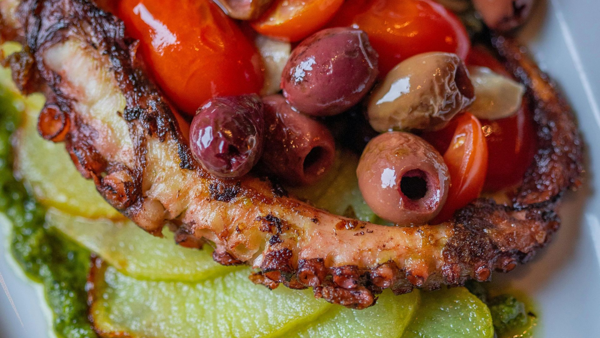 Kalamata olives and grilled octopus served on charred vegetables, traditional Greek food in Athens