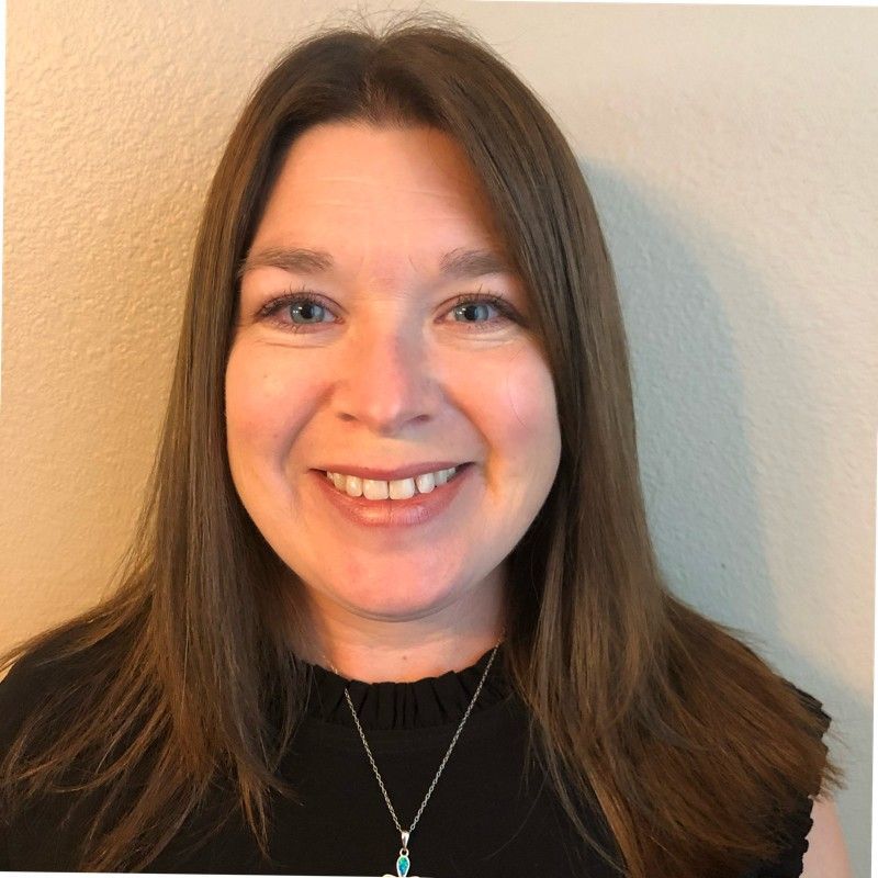 A woman wearing a black shirt and a necklace is smiling for the camera.