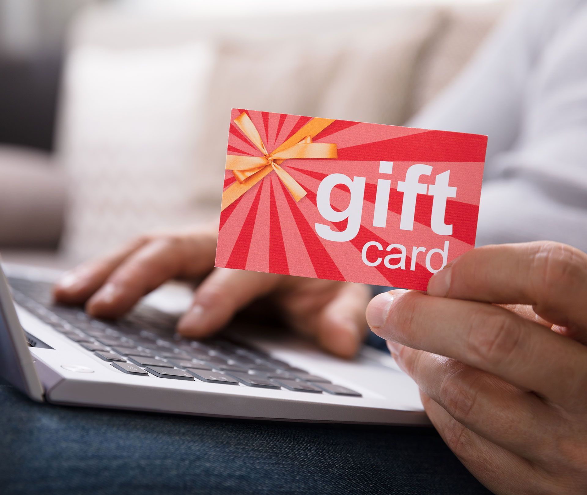 A person is typing on a laptop while holding a gift card