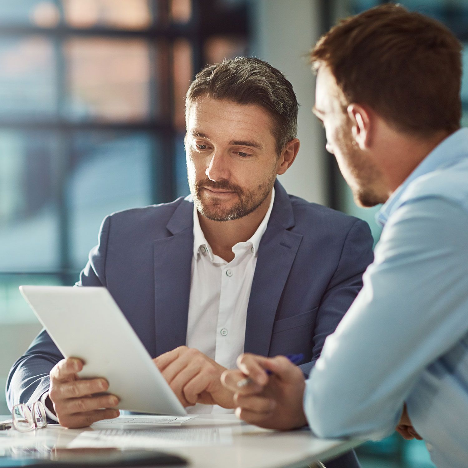 Two men are sitting at a table looking at a tablet.