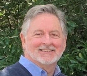 A man with a beard and a blue shirt is smiling for the camera.