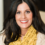 A woman wearing a yellow scarf and a sweater is smiling for the camera.