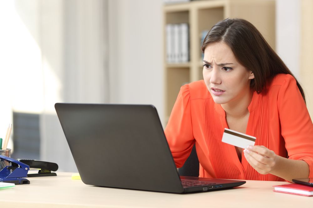 A woman is holding a credit card while using a laptop computer.