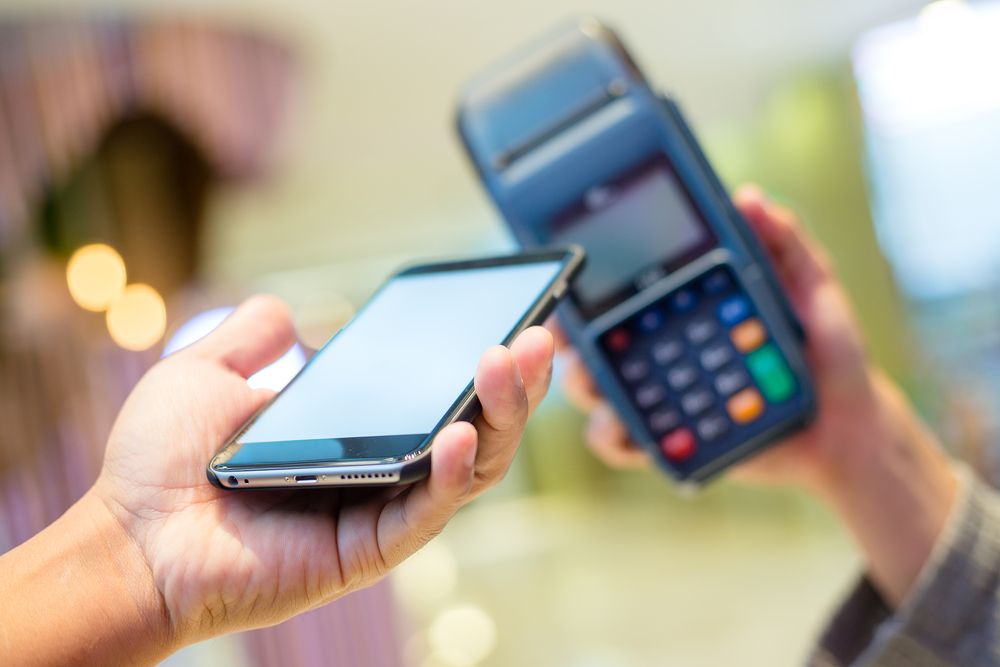 A person is holding a cell phone in front of a credit card machine.