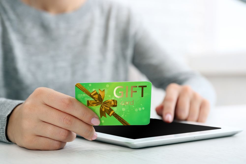 A person is holding a green gift card in front of a tablet.