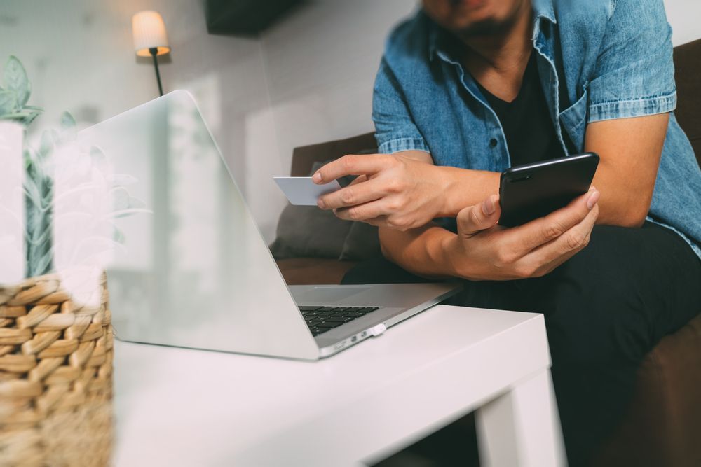 A man is sitting on a couch using a laptop and a credit card.