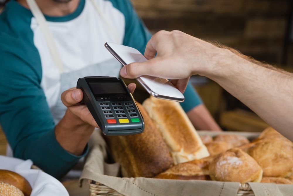 A man is using a credit card to pay for bread in a bakery.