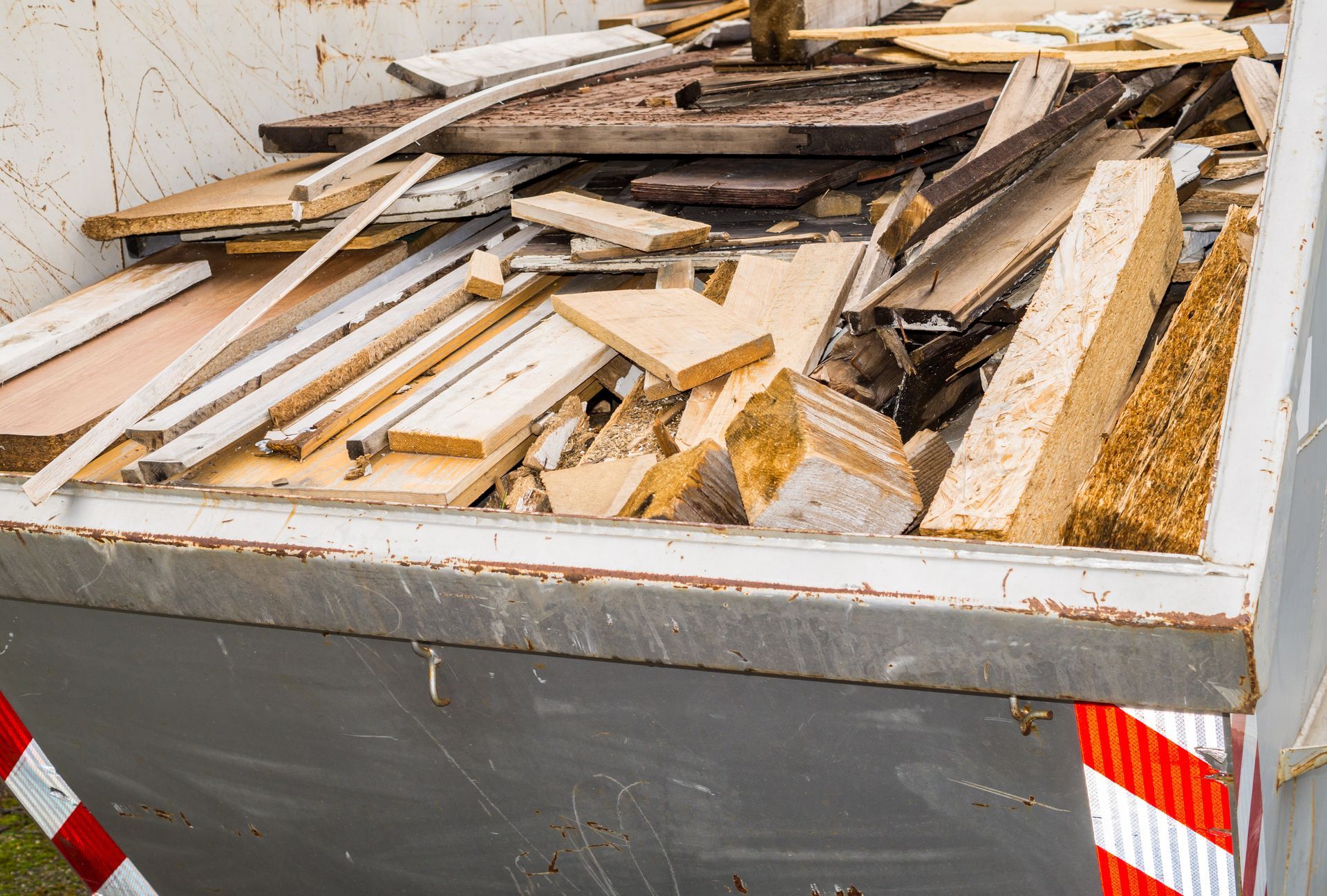 A grey dumpster filled with assorted construction debris, including wooden boards, panels, and fragments.