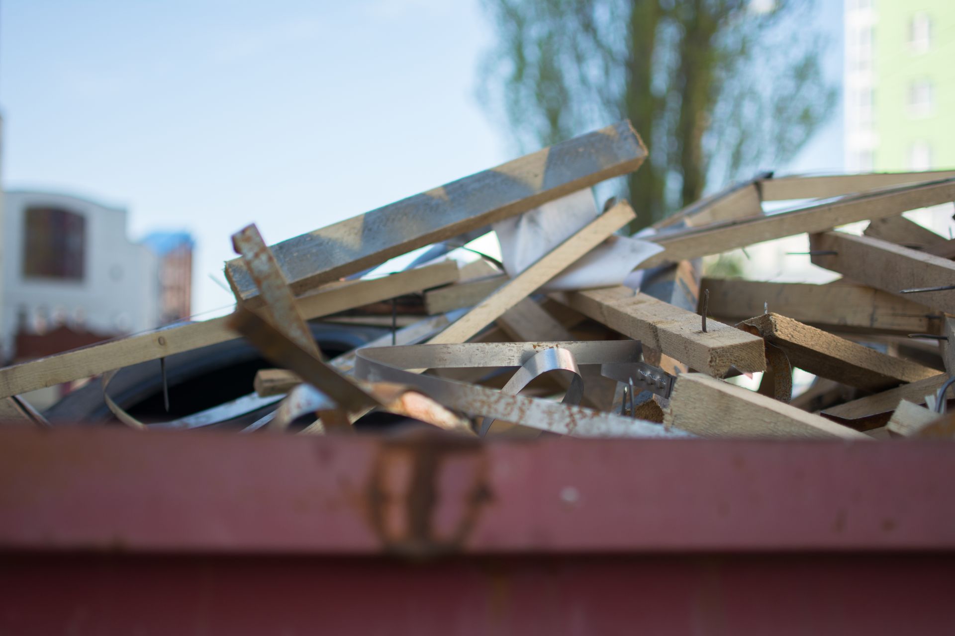 A close-up view of a red metal dumpster filled with discarded wooden boards and debris under a clear blue sky.