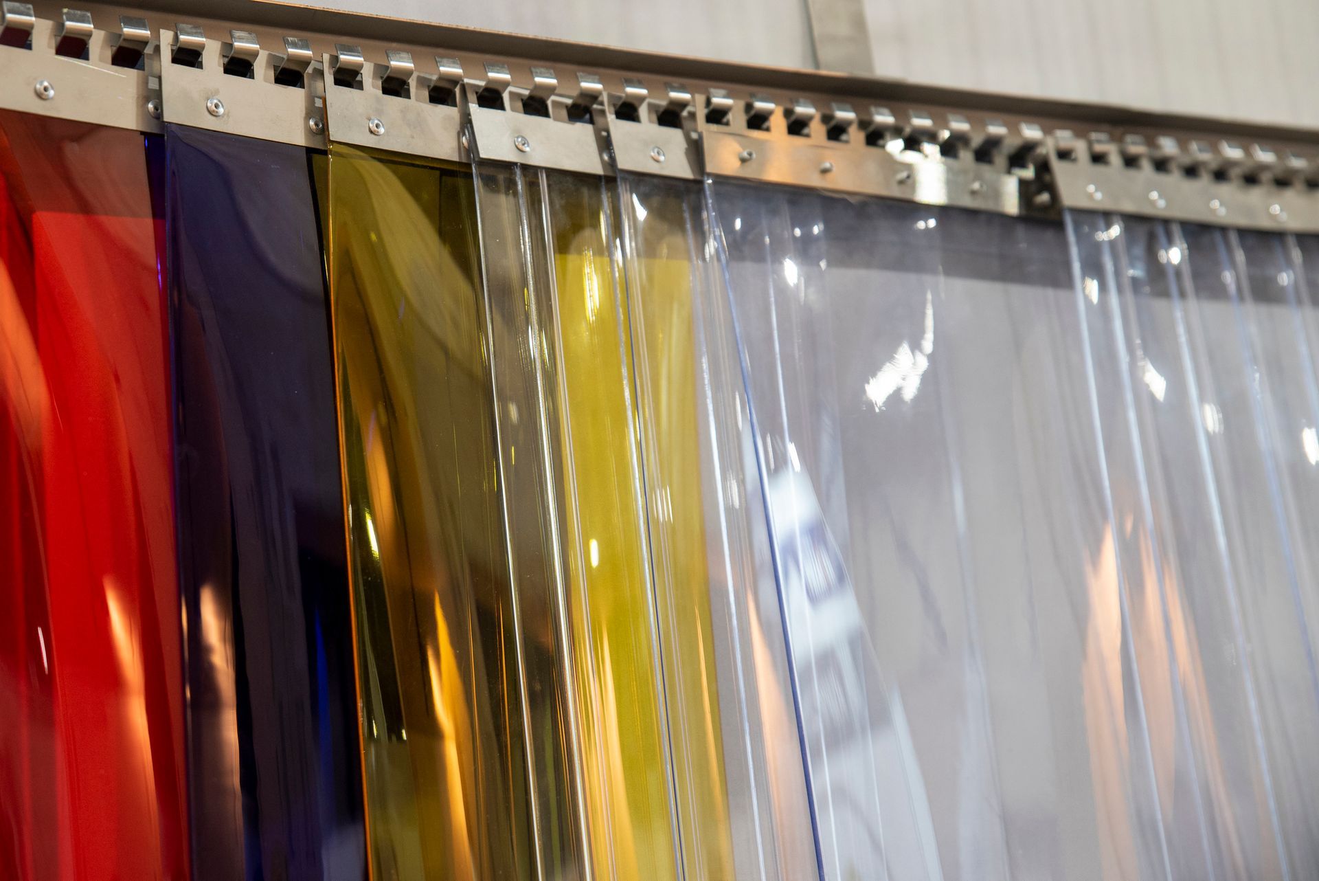 Plastic strip curtains of varying colors hanging from a metal track; includes red, blue, amber, yellow, and clear strips.