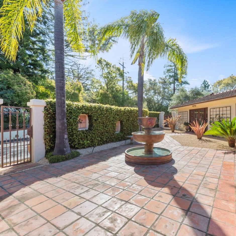 A patio with a fountain and palm trees in front of a house.