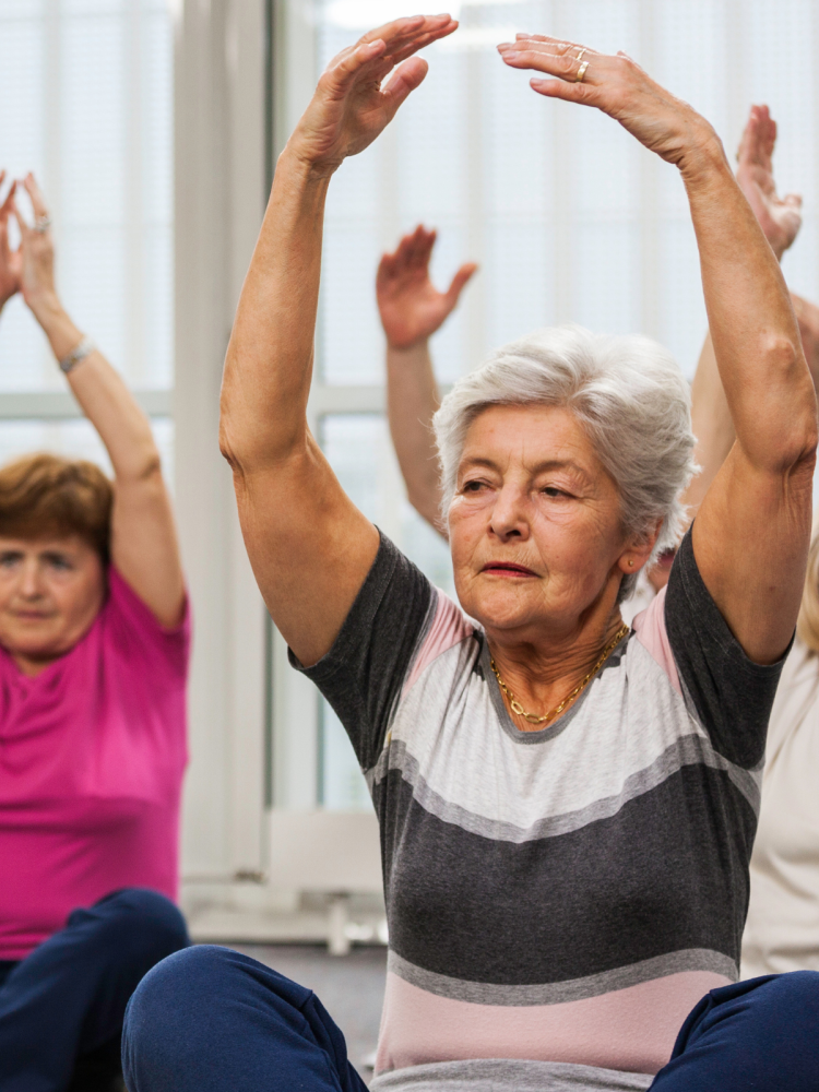 A group of older women are sitting on the floor with their arms in the air.