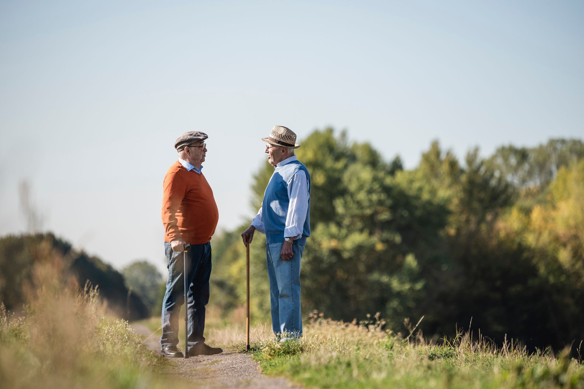 Two men are standing on a dirt road talking to each other.