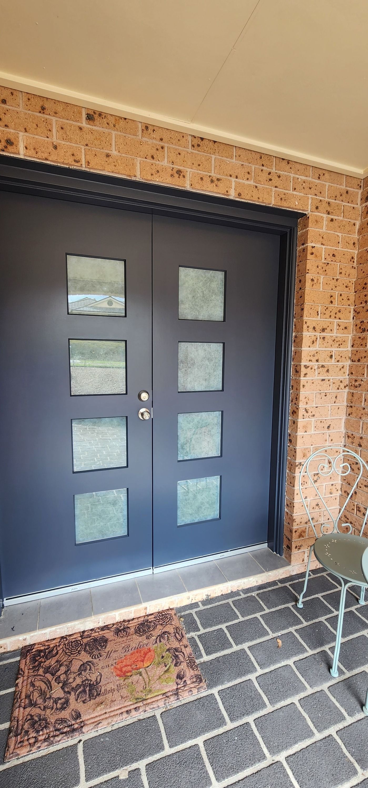 A Black Door With Square Windows is Sitting on a Brick Porch — JAX Painting Services in Central Coast, NSW